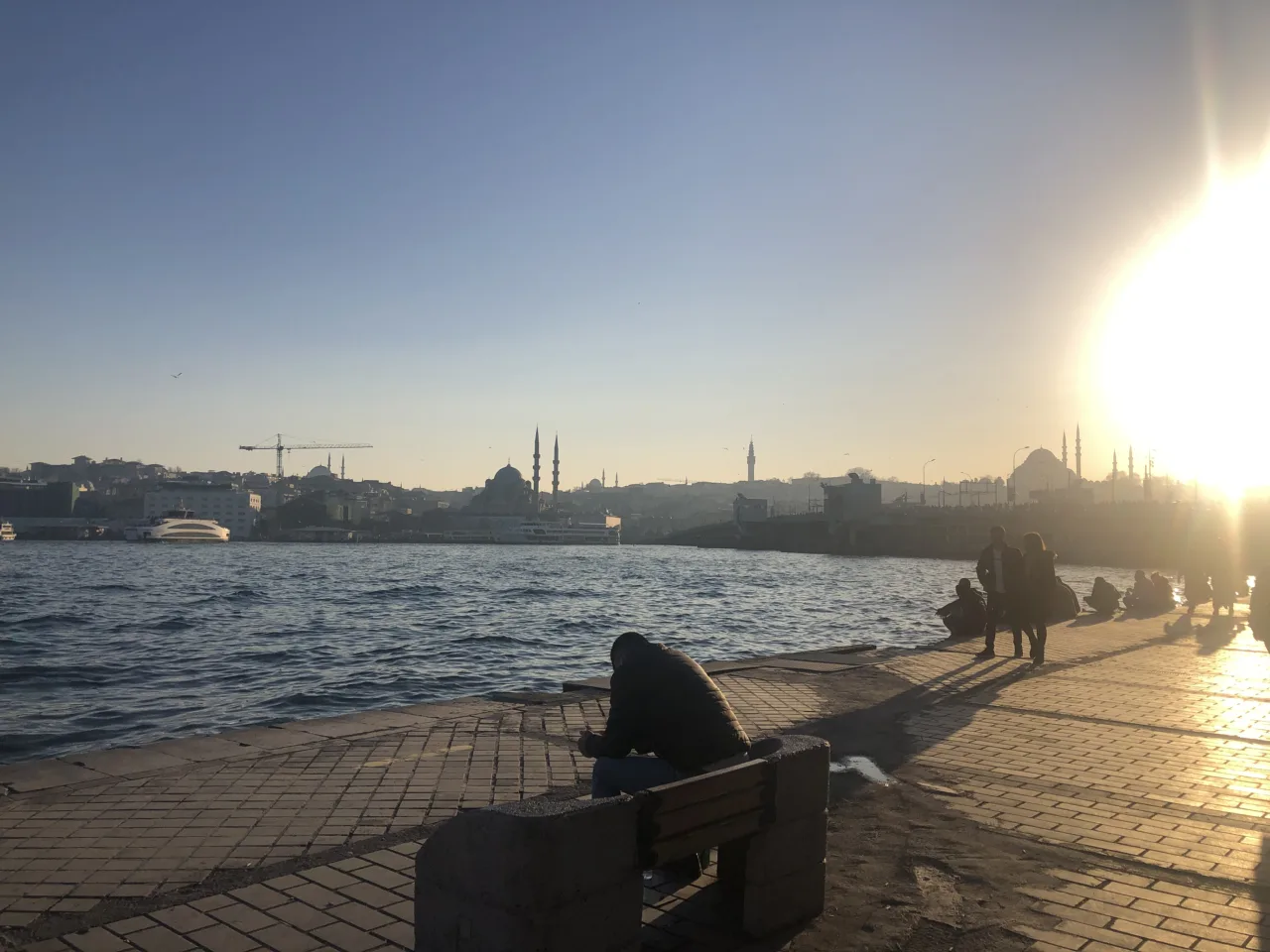 Paseo junto al Cuerno de Oro al atardecer, con bancos y la silueta de Estambul al fondo.