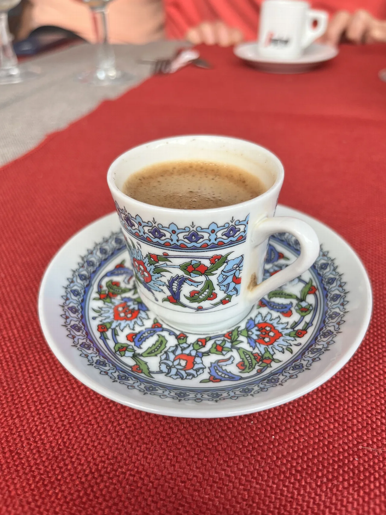 Taza de café turco en un plato decorado sobre una mesa roja.